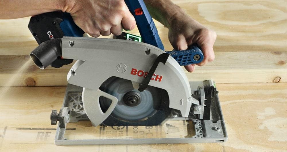 Person using Bosch circular saw mounted on guide rail to cut plywood; blade spinning and sawdust visible.