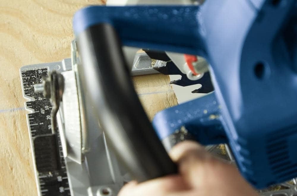 Close-up of Bosch circular saw cutting plywood with metal guide attached for precise measurement and alignment.