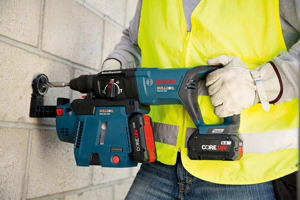 Person using Bosch Bulldog rotary hammer drill with dust extractor to drill into concrete block wall; wearing safety vest and gloves.