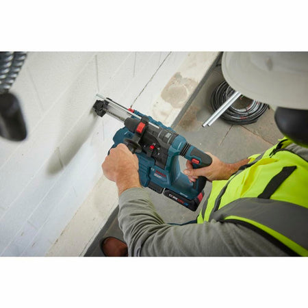 Construction worker in high-visibility vest drilling into a white masonry wall using the Bosch 18V Bulldog Rotary Hammer for concrete drilling, demonstrating its cordless maneuverability.