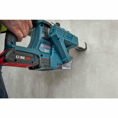 Close-up of a worker using the Bosch 18V Bulldog Rotary Hammer in hammer-only mode with a dust extractor attachment, chipping masonry or tile off a wall, demonstrating compliance and versatility.