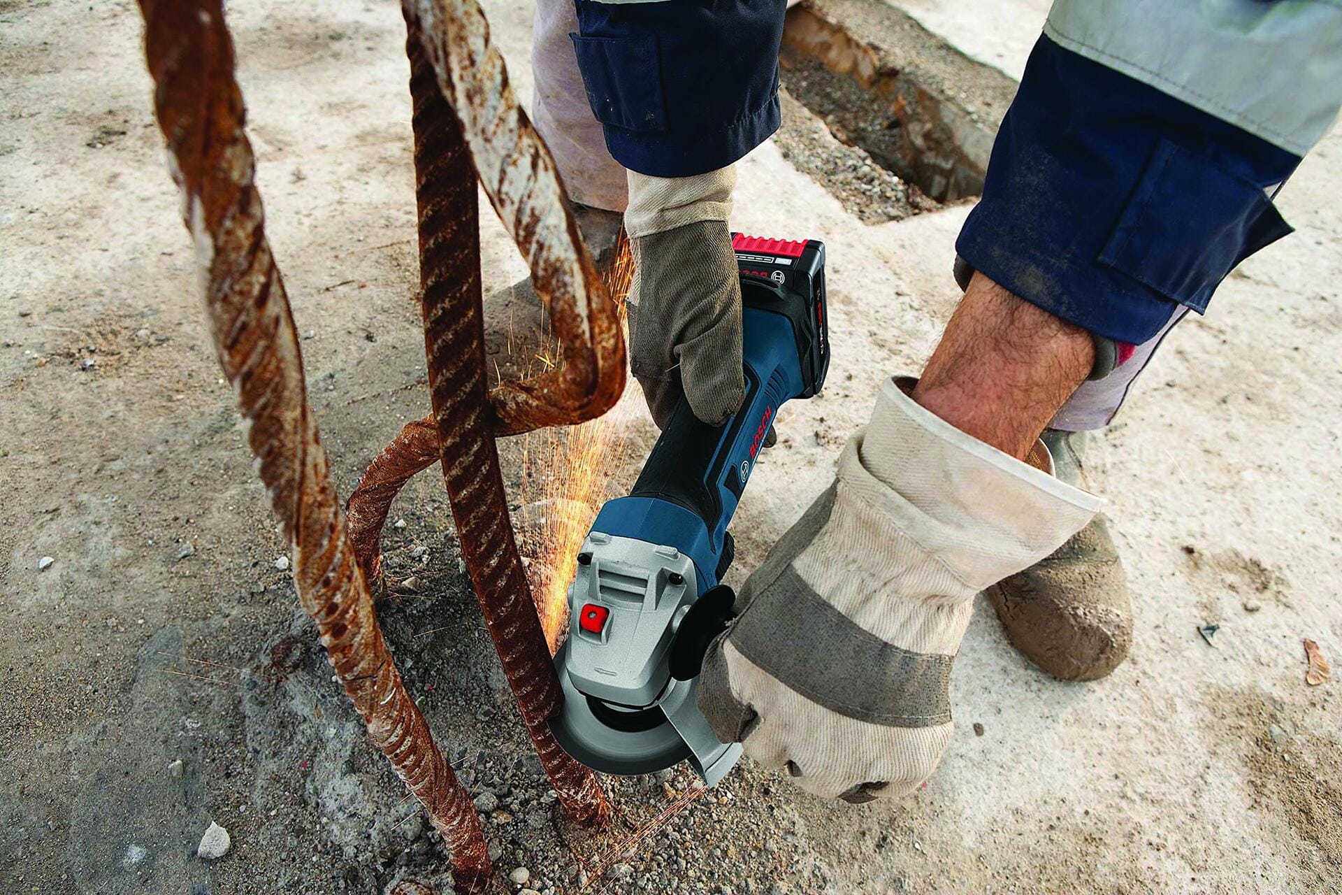 Worker using Bosch cordless angle grinder to cut rusted rebar embedded in concrete; sparks visible during active cutting on jobsite.