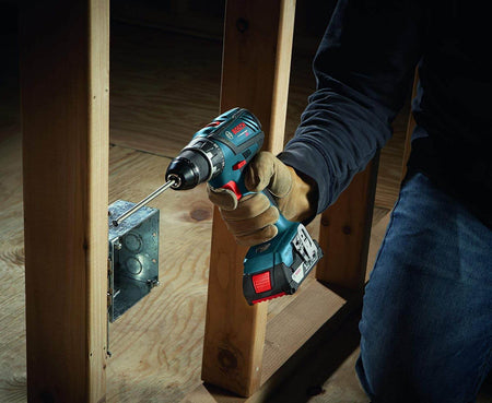 Worker using a Bosch 18V cordless drill driver to secure a metal electrical box between wall studs, demonstrating compact tough performance, ergonomic handling, and reliable fastening power for framing and electrical installation tasks.