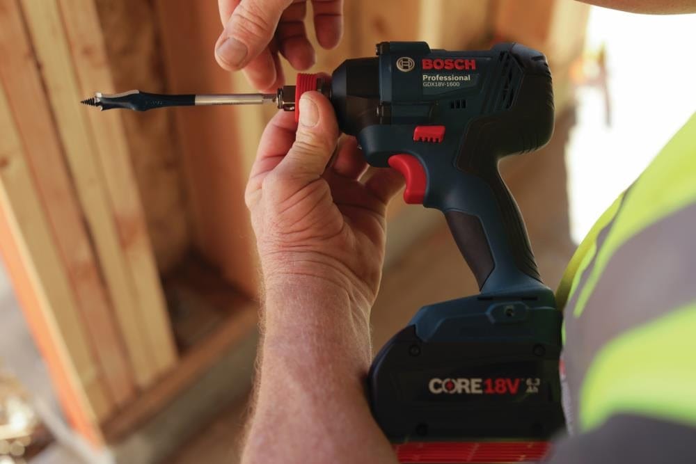 Close‑up of a Bosch 18V GDX18V‑1800 2‑in‑1 impact driver as a worker inserts a hex‑shank spade bit, highlighting quick‑change versatility, CORE18V battery power, and precision setup for drilling and fastening in construction environments.