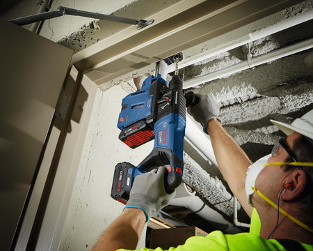 Action shot of a construction worker using the Bosch GBH18V-26D rotary hammer for overhead concrete drilling into a ceiling, demonstrating the tool's performance in tight jobsite conditions
