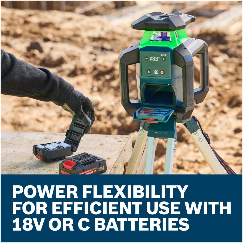 A surveyor wearing rugged work gloves prepares the Bosch self-leveling transit tool on an active dirt construction site. The user chooses between power options, with an open alkaline battery adapter cartridge and an 18V lithium-ion battery pack resting side-by-side on a wooden plank.