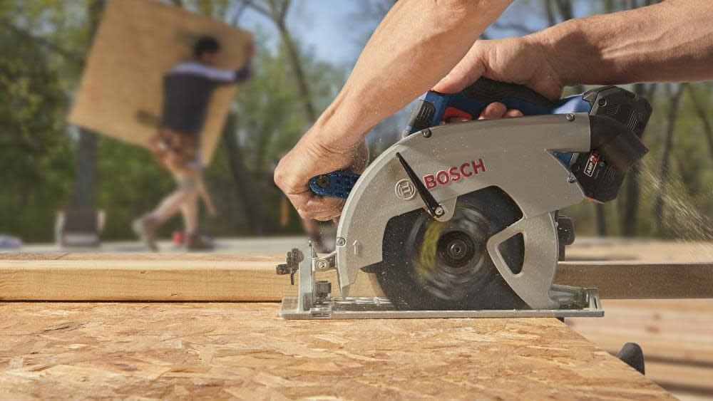 Close-up of Bosch circular saw cutting OSB board; sawdust flying as person works on outdoor construction site.