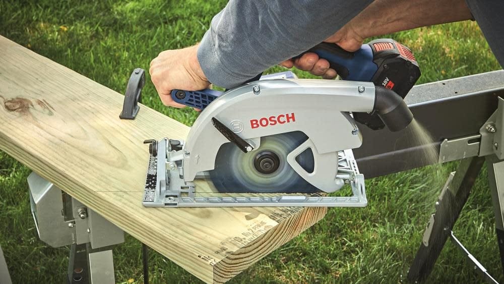 Person using Bosch circular saw to cut lumber on metal sawhorse outdoors; spinning blade in contact with wood.