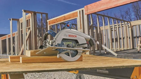 Bosch circular saw resting on wooden planks at construction site; partially built frame structure visible in background.