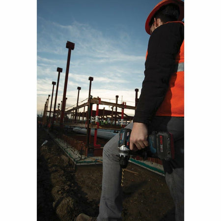 Person holding a power drill on a construction site with a blue sky and cranes in the background.
