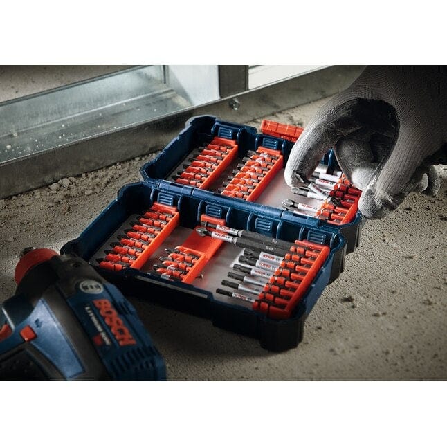 The open Bosch SDMS24 Custom Case rests on a metal stud at a construction site, while a worker in the background uses an impact driver.