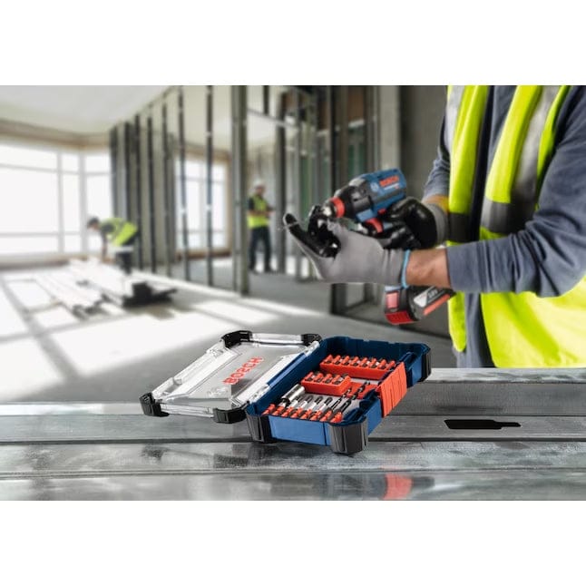 A gloved hand takes a screwdriver bit from the open Bosch SDMS24 case, which is resting on a concrete floor next to an impact driver.