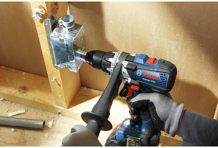 An action shot of a worker using a Bosch cordless drill and a step drill bit to enlarge a hole in a metal electrical junction box.