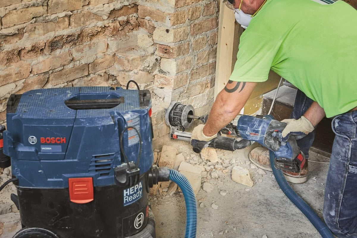 An on-site construction image of an operator utilizing a Bosch cordless rotary hammer equipped with an SDS-Plus chisel and dust extraction shroud to chip away structural brick masonry, with a Bosch HEPA-ready dust extractor vacuum managing jobsite silica particles.