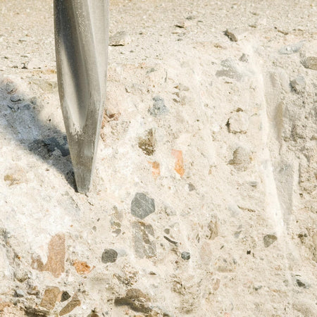 A macro detail shot of a Bosch self-sharpening star-point twist chisel fracturing a dense, stone-filled structural concrete slab to demonstrate high-impact demolition performance.