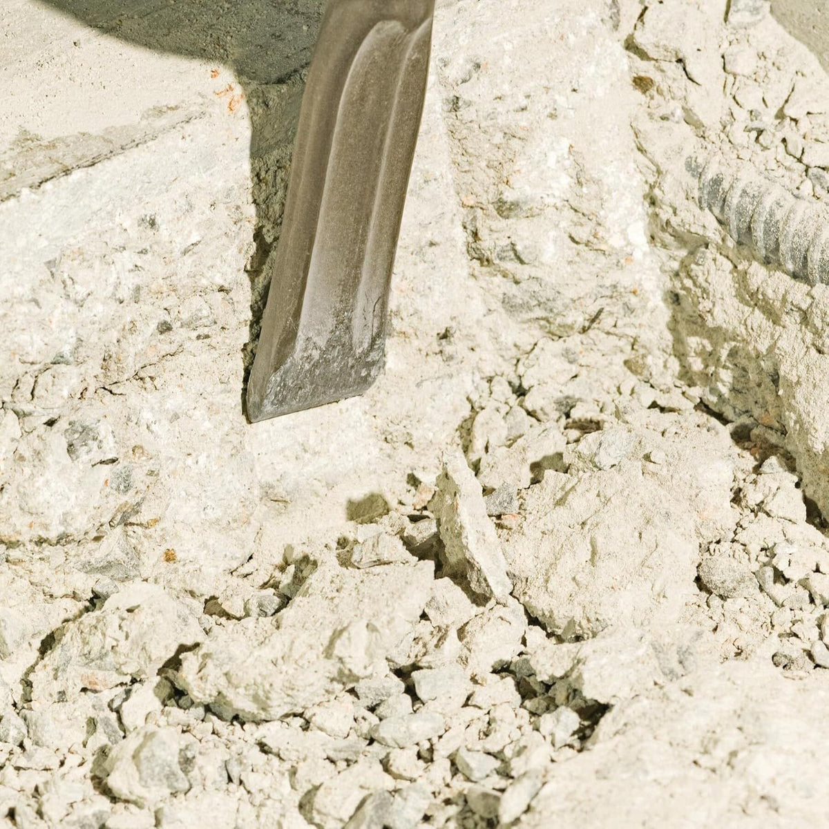 A macro shot showing a Bosch self-sharpening flat viper chisel digging into concrete rubble and stone aggregate, illustrating effective material removal and low-friction line chiseling.