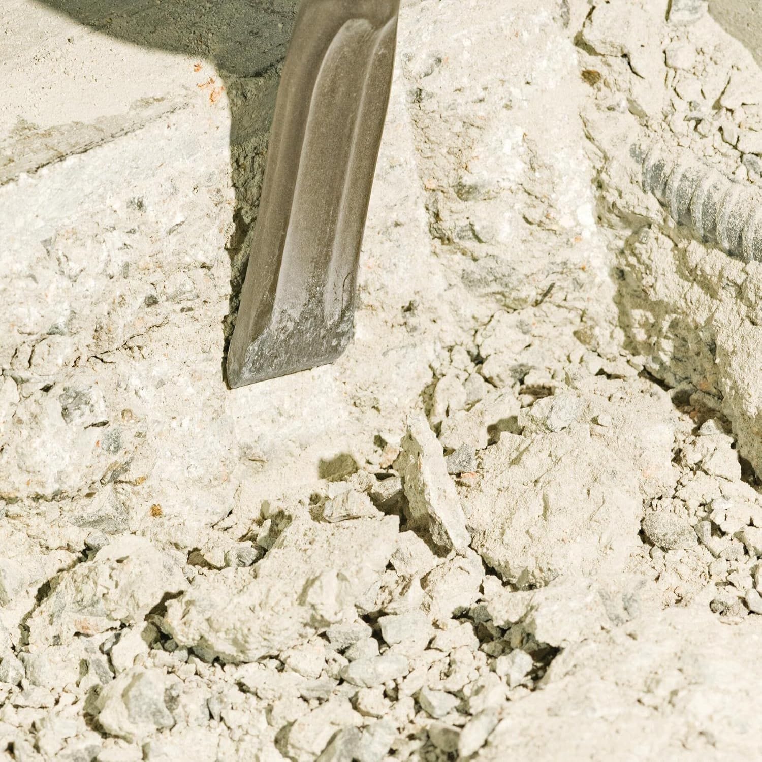 A macro shot showing a Bosch self-sharpening flat viper chisel digging into concrete rubble and stone aggregate, illustrating effective material removal and low-friction line chiseling.