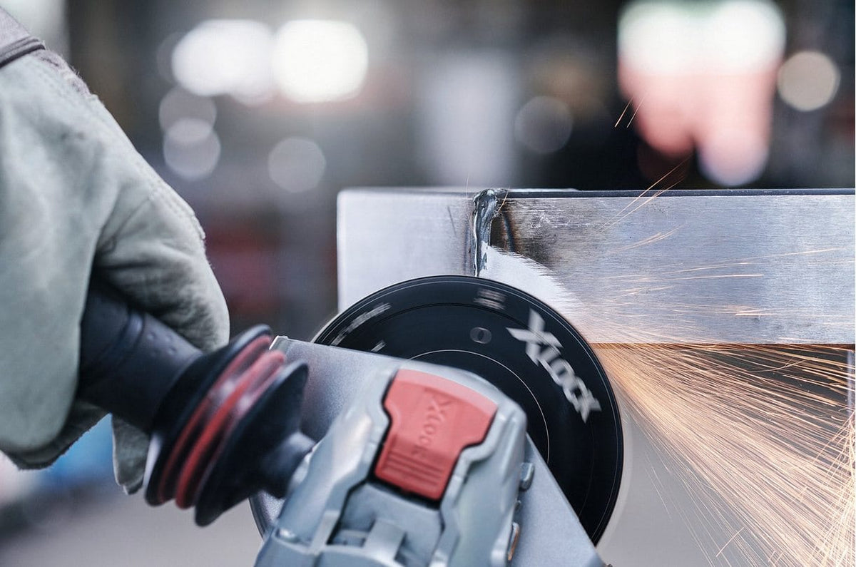 Bosch angle grinder with X-LOCK disc actively grinding metal corner; sparks visible and glove worn for safety.
