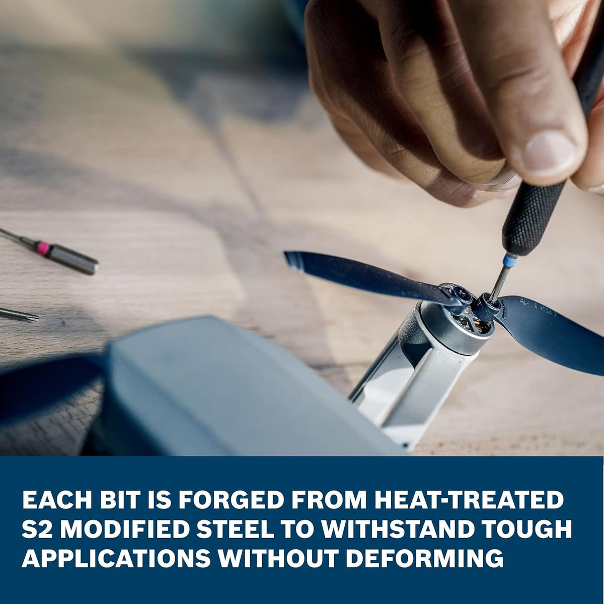 A detailed view of a repair specialist performing intricate maintenance on a miniature drone motor using a precision tool from the Bosch PB4042 set. Infographic text underlines the durability of the heat-treated S2 modified steel bits engineered to withstand repeated mechanical use.