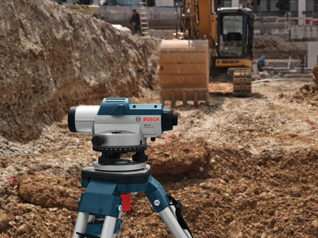 Bosch GOL 32 optical level mounted on tripod in front of excavator; urban construction site in background.