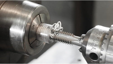 A close-up macro action shot of a Bosch tap in a lathe, cutting threads into a round metal workpiece.