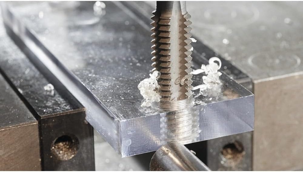 A close-up macro action shot of a Bosch tap cutting threads into a pre-drilled hole in a clear acrylic block held in a vise.