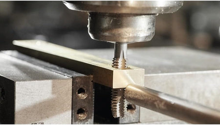 A close-up macro action shot of a Bosch tap cutting threads into a pre-drilled hole in a brass bar.