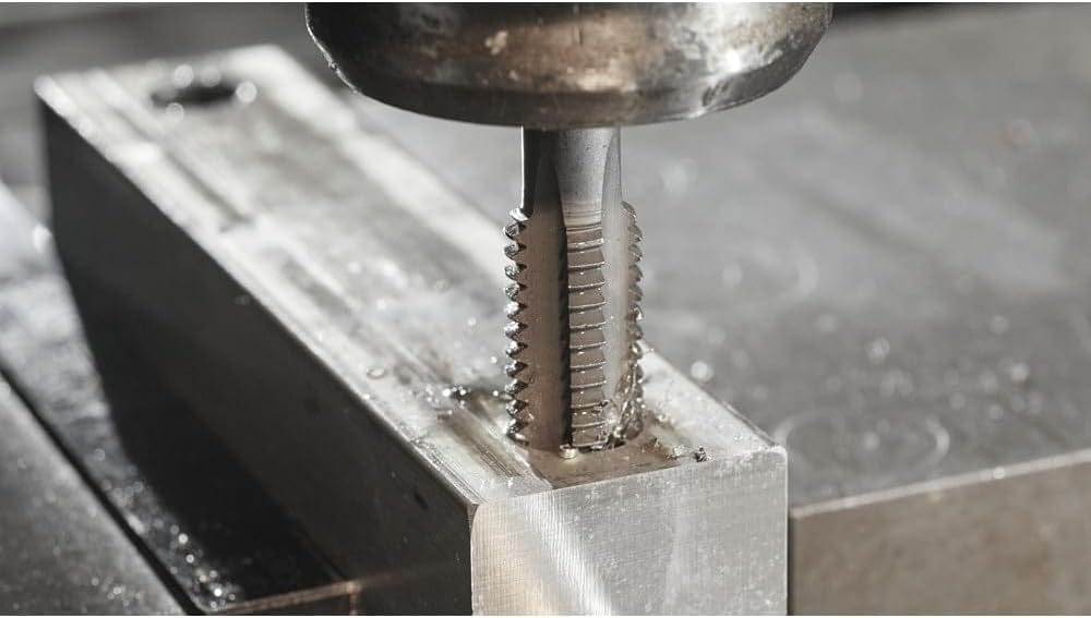 A close-up macro action shot of a Bosch tap cutting threads into a pre-drilled hole in a metal block.
