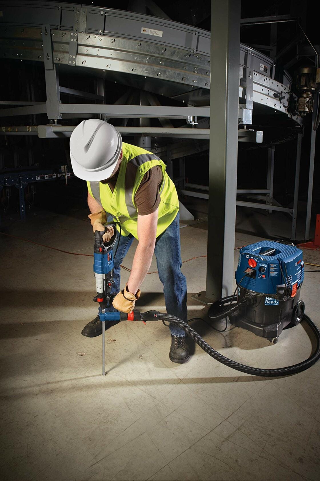 Construction worker using Bosch rotary hammer drill with dust extraction system to drill into concrete floor in industrial setting