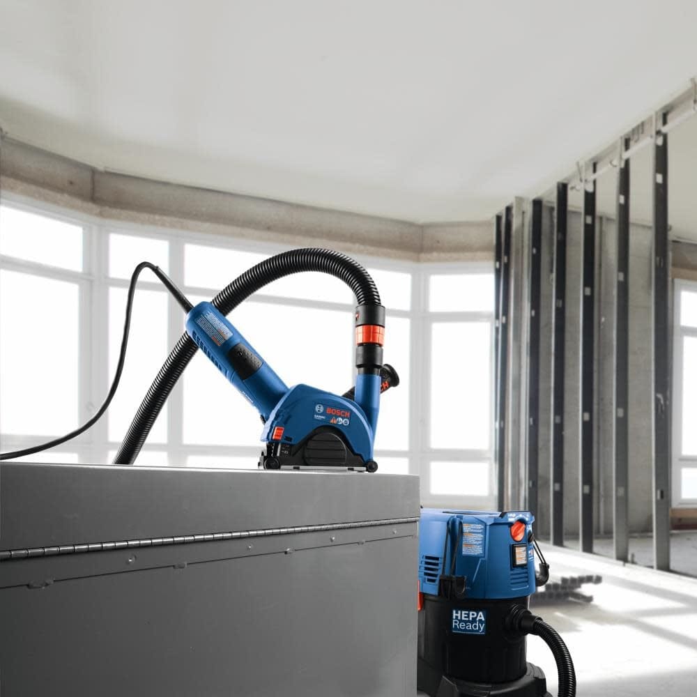 Bosch power tool connected to HEPA vacuum system in a construction site with exposed metal wall studs.