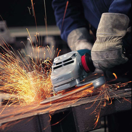 Person using angle grinder on metal surface with bright sparks; protective gloves worn in industrial setting.