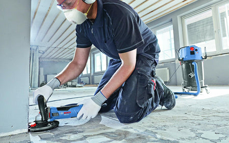Worker using Bosch DC530SG 5 In. Turbo Diamond Cup Wheel For Concrete on floor surface in a renovation setting