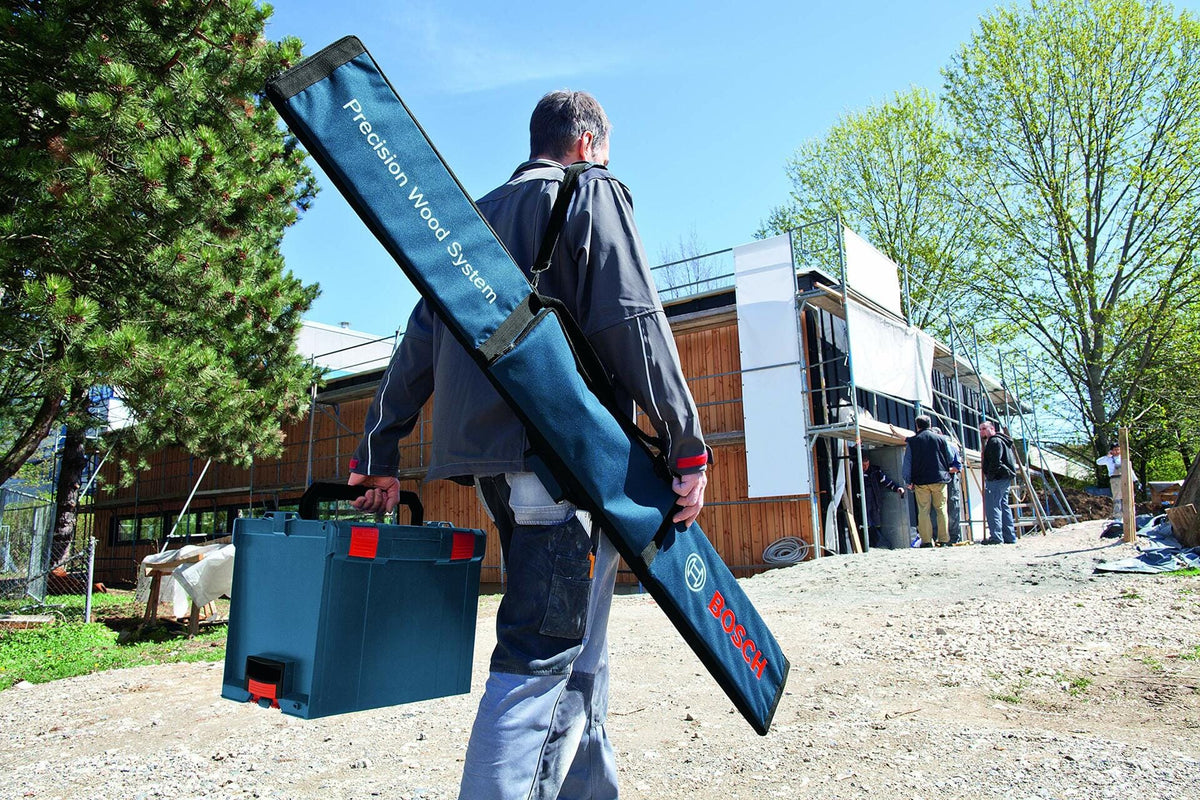 A construction worker carries the Bosch track saw guide rail kit in its blue bag slung over his shoulder while walking onto a jobsite.