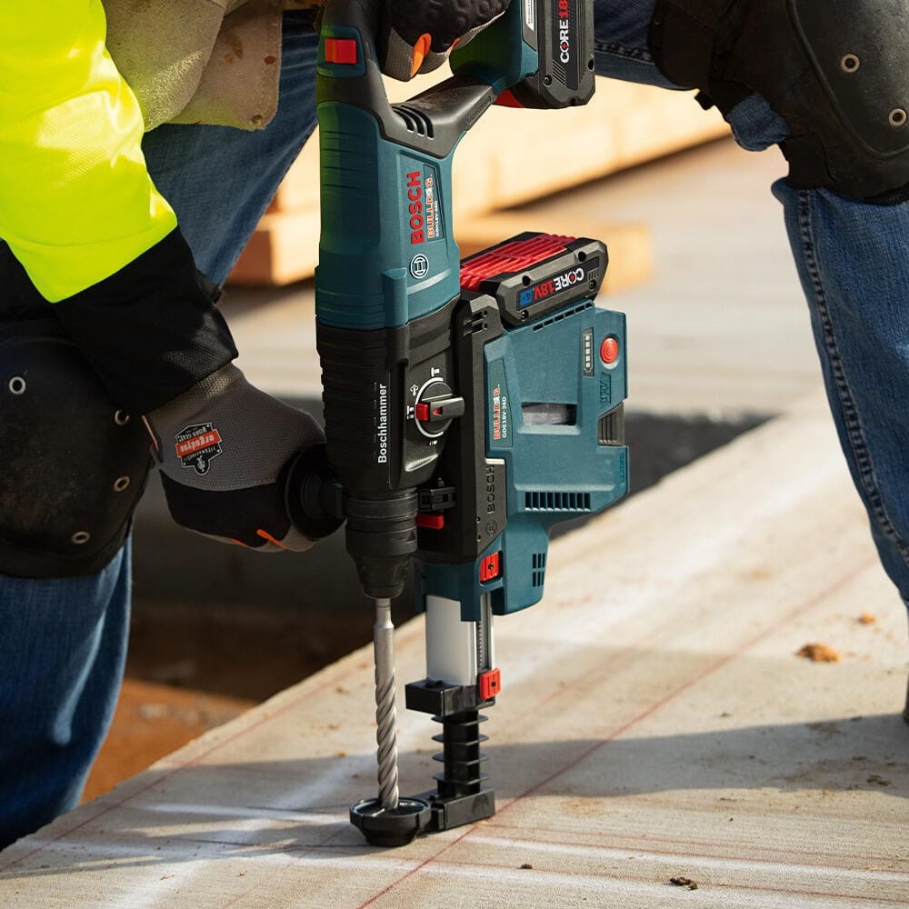 A detailed close-up shot of a contractor utilizing a Bosch 18V cordless rotary hammer drill with an onboard vacuum dust collection collector to bore precise, code-compliant anchor holes downward into a chalk-lined concrete deck using a four-flute spiral masonry bit.