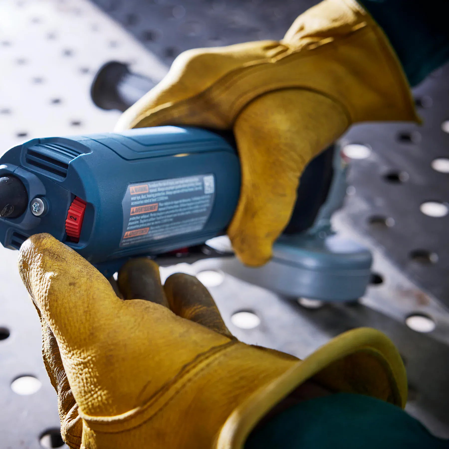 Operator adjusting the rear variable speed dial on the Bosch GWS12-450PBD angle grinder housing.