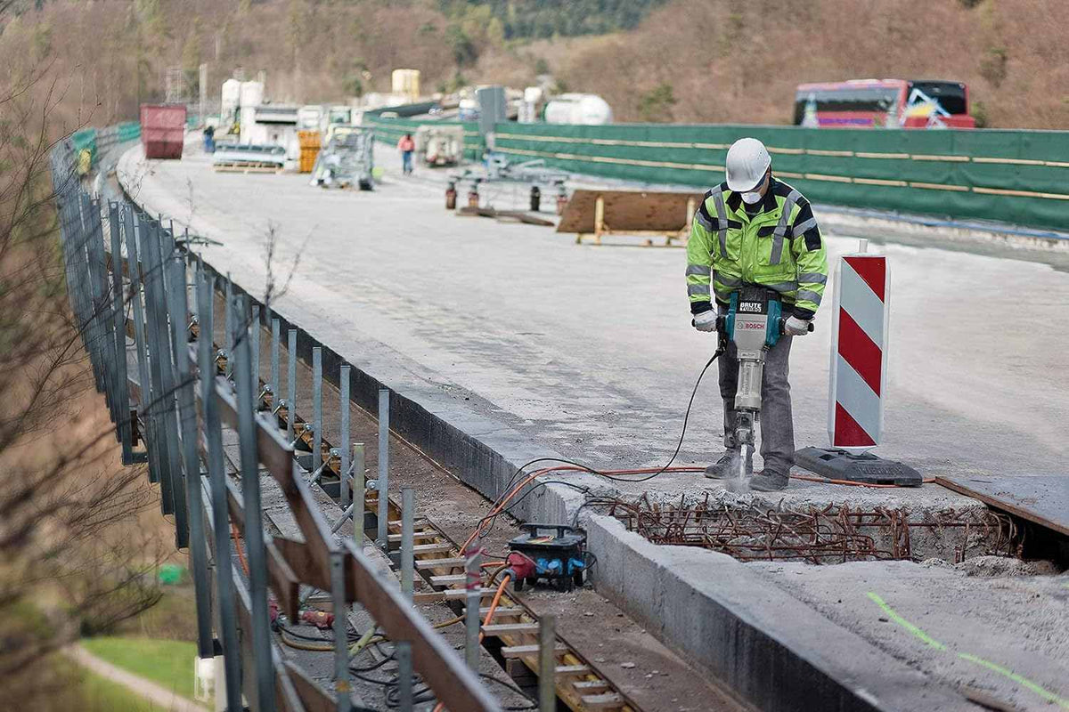 A professional contractor in a high-visibility jacket operates the Bosch Brute Turbo hex concrete demolition hammer to break up a thick concrete bridge deck on an outdoor highway construction site.