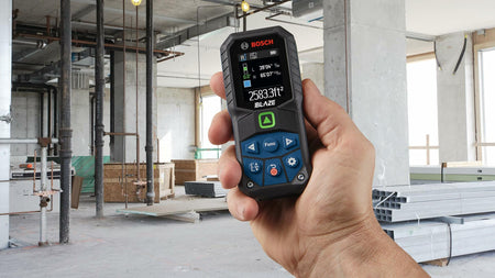 Action shot showing a hand holding the Bosch GLM165-27CGL laser measure on a construction site, with the color display showing a large calculated area measurement of 2583.3 square feet