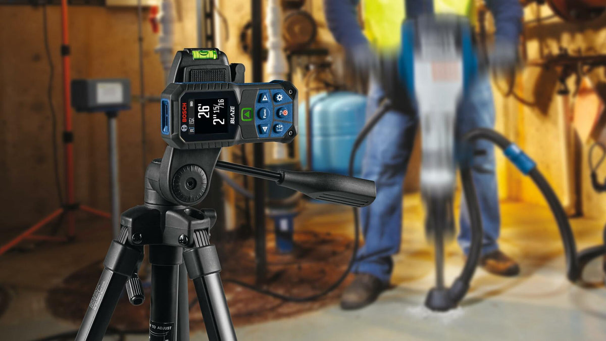 Action shot showing the GLM165-27CGL laser measure mounted on a tripod for stable measurements in an industrial environment, with a construction worker drilling concrete in the background