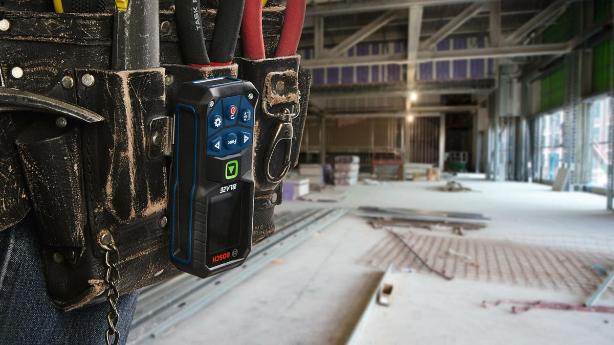 Action shot showing the Bosch GLM165-27CGL laser measure securely clipped to a worker's tool belt, illustrating the use of the belt clip for convenient jobsite portability