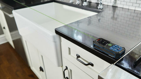 Action shot showing the Bosch GLM165-27CGL green laser measure sitting on a countertop, projecting the highly visible green laser beam across a sink to take an accurate indoor measurement
