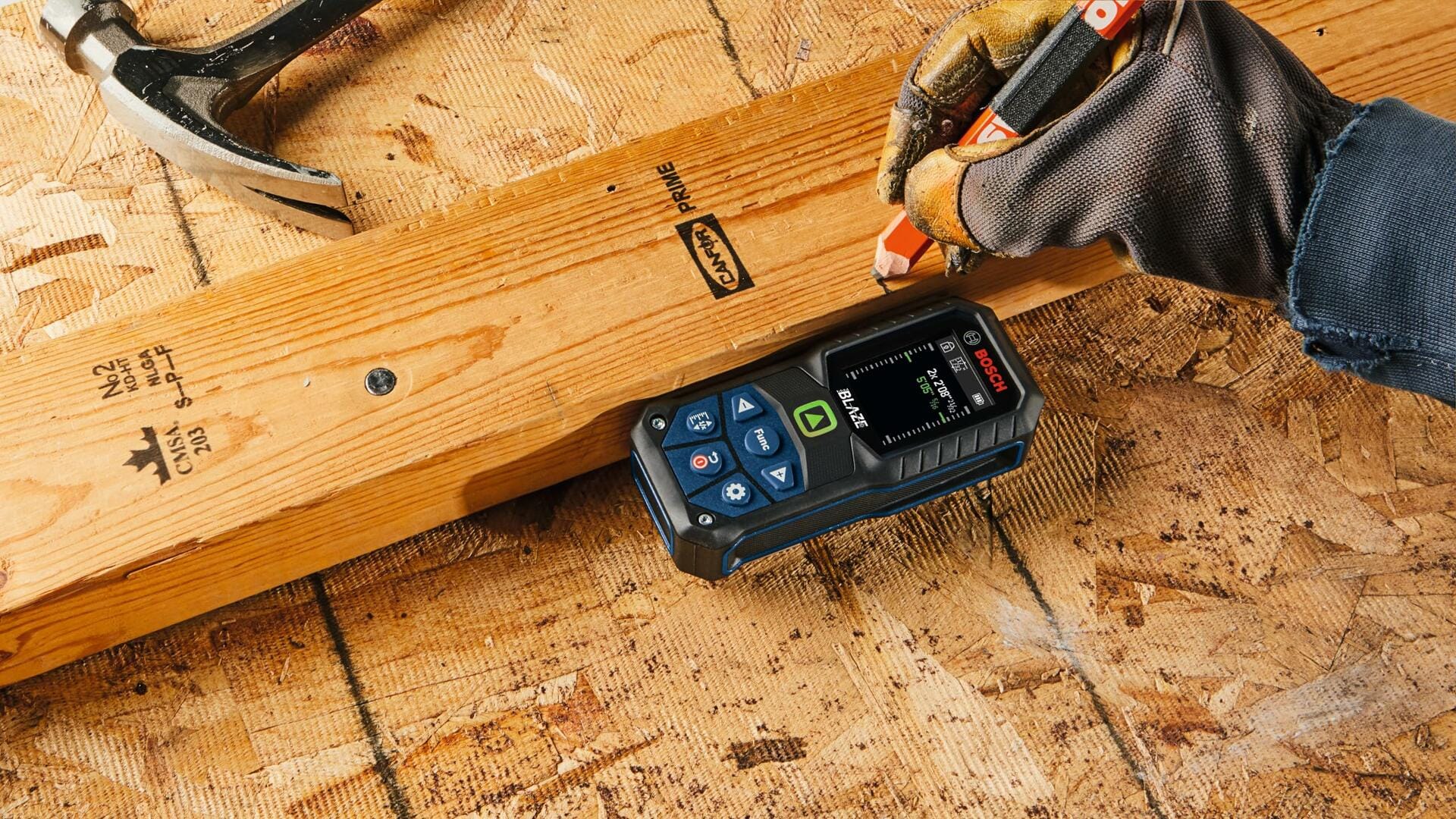 Overhead action shot of a worker using the laser measure on a 2x4 piece of lumber, marking the wood with a pencil to transfer a measurement during construction layout