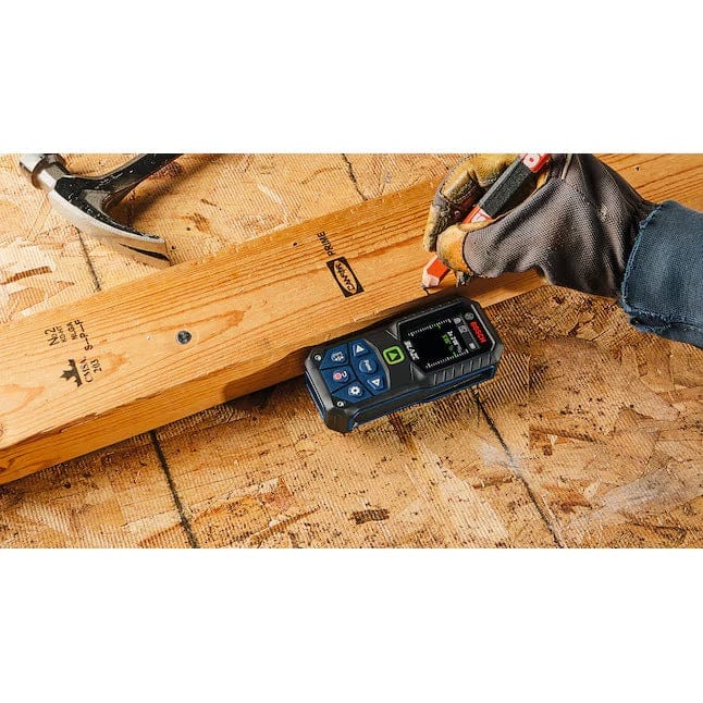 Overhead action shot of a construction worker using the Bosch GLM165-27CG laser measure to measure and mark a line on a 2x4 piece of lumber on a construction site floor
