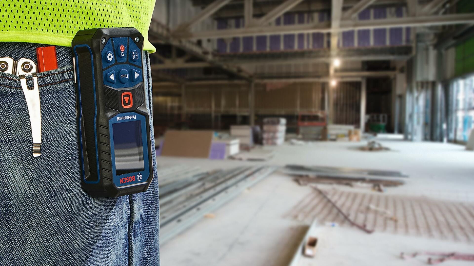 BOSCH GLM165-22 laser distance measure attached to worker’s belt inside a large unfinished construction site