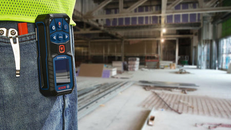 BOSCH GLM165-22 laser distance measure attached to worker’s belt inside a large unfinished construction site