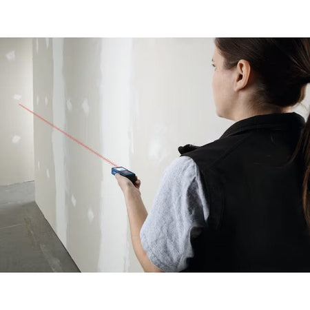 Rear view of a worker using the Bosch GLM165-10 to project a red laser beam across an indoor construction area for quick and accurate wall-to-wall measurements.