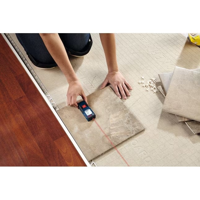 A professional using the Bosch BLAZE One laser measure on a tile floor to ensure precise alignment and layout during a flooring renovation.