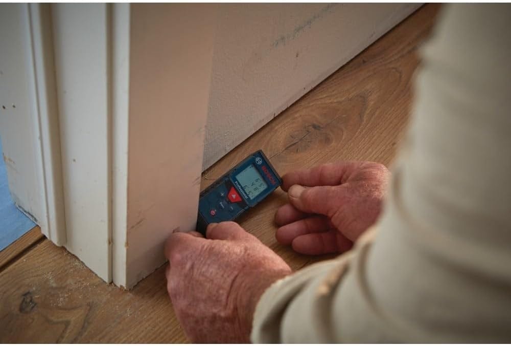An action shot of a professional user using the Bosch GLM165-40 laser distance measure to quickly capture an accurate wall-to-floor dimension at the base of a doorway.