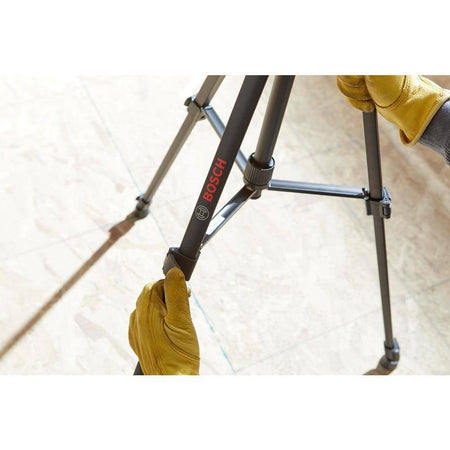 Person wearing yellow gloves adjusting leg lock on Bosch BT 150 tripod placed on light-colored flooring