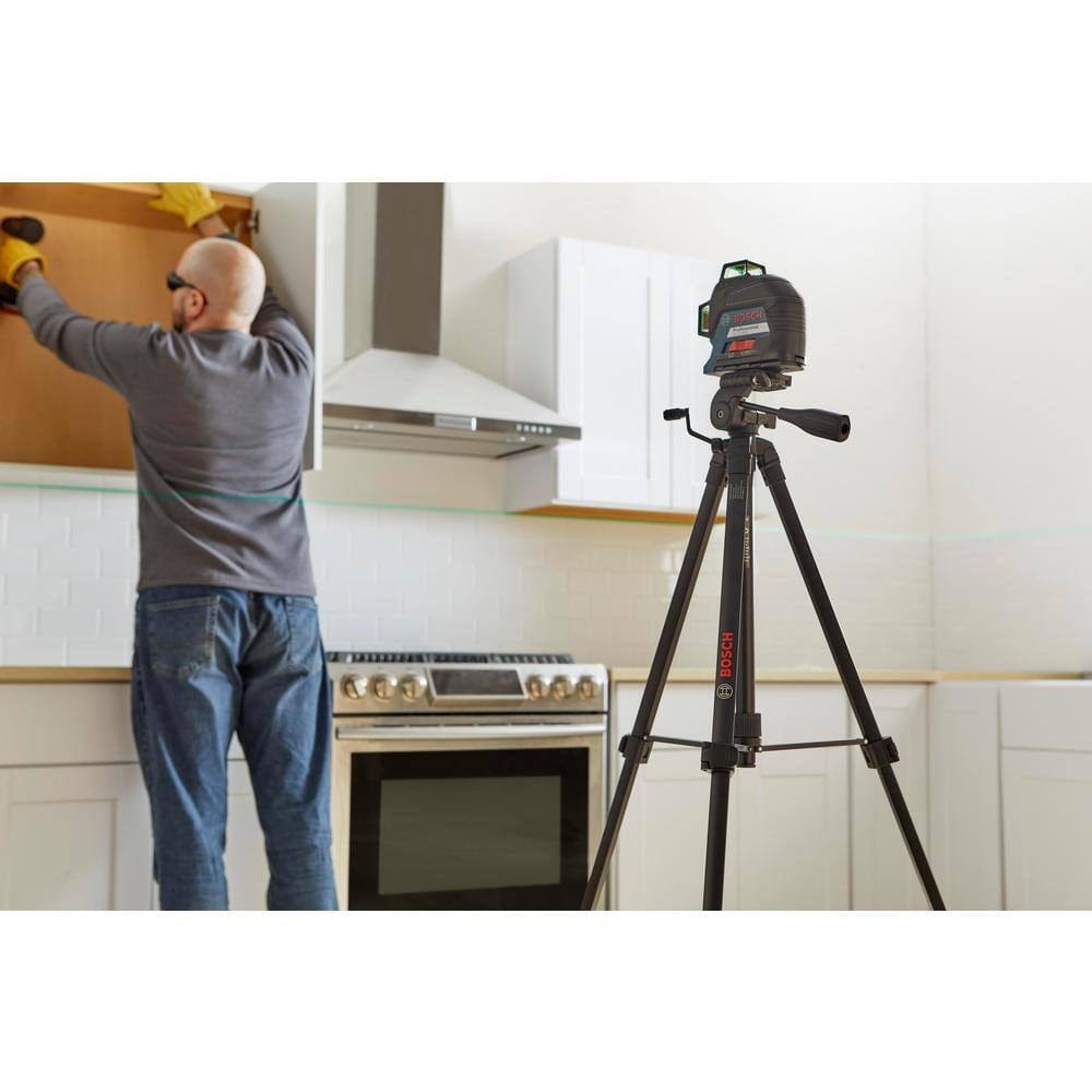 Person using Bosch BT 150 tripod with mounted laser level projecting green line to align kitchen cabinet installation.