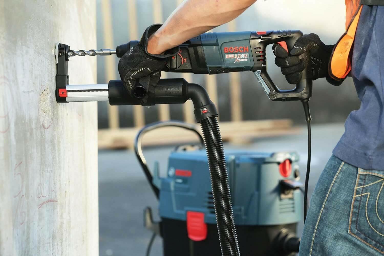 The Bosch Bulldog rotary hammer is shown attached to a PRO+GUARD dust extraction system, drilling horizontally into a concrete wall.